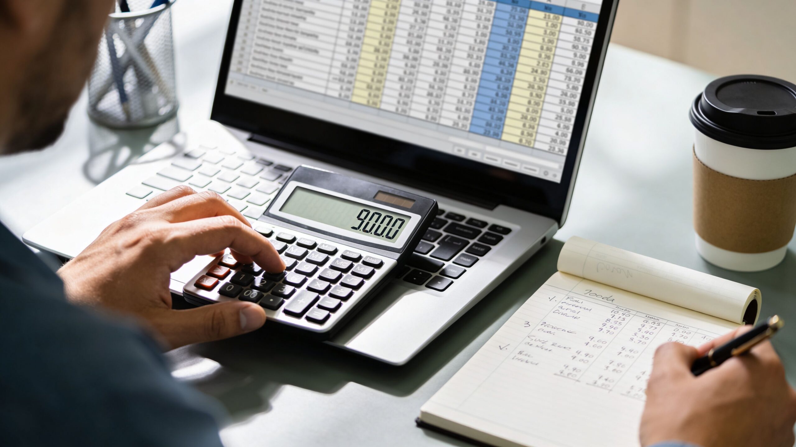 Un contable calculando gastos financieros mientras trabaja con una hoja de cálculo digital y una libreta