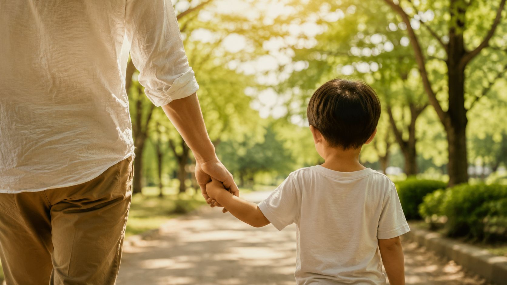 Un padre caminando de la mano con su hijo pequeño en un parque durante un día soleado.